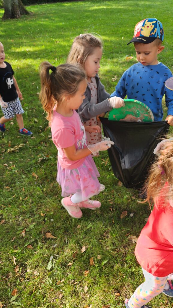Na zdjęciu dziewczynki wrzucają plastikową pokrywkę do worka na śmieci 
