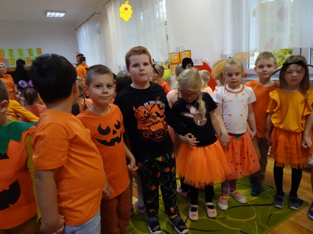Dzieci w pomarańczowych ubraniach, ustawione w rzędzie.