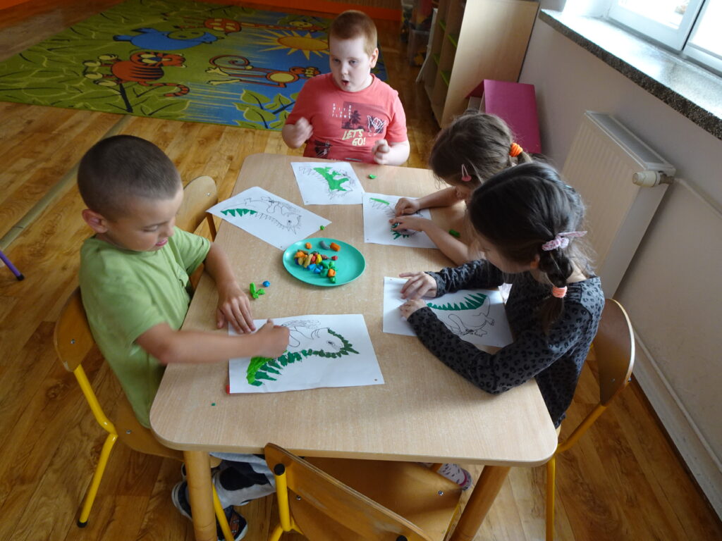 Dzieci przy stoliku, podczas lepienia plasteliną. 