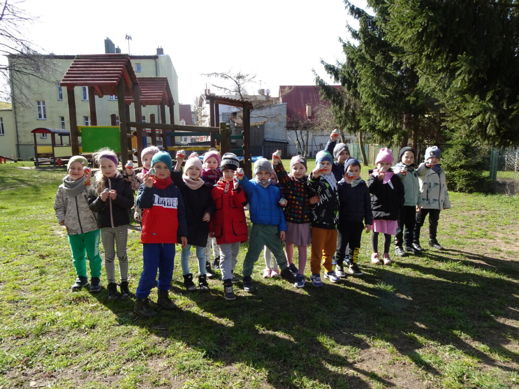Zdjęcie grupowe, na ogrodzie przedszkolnym. Dzieci trzymają w rączkach czekoladowe jajka. 