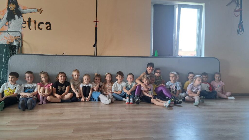 Zdjęcie grupowe. Dzieci siedzą na podłodze z panią instruktor ze szkoły tańca. 