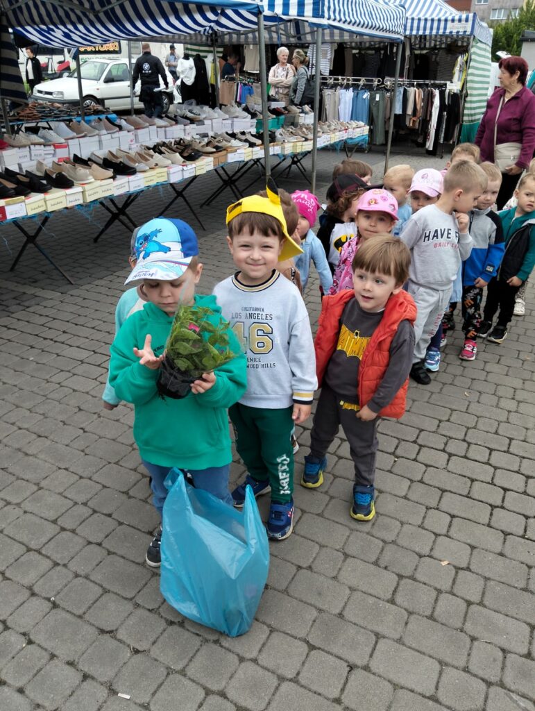 Zdjęcie na rynku. Dzieci ustawione w parach. W tle widać stragany. 