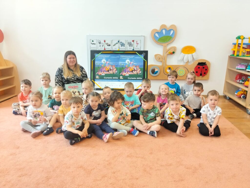 Zdjęcie grupowe z panią bibliotekarką. Dzieci siedzą na dywanie. 