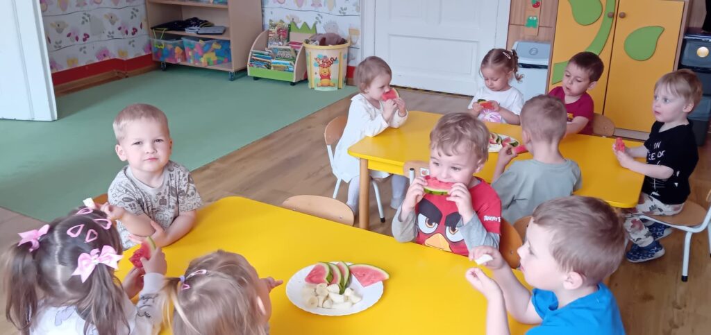 Dzieci przy stoliku podczas jedzenia owoców. 