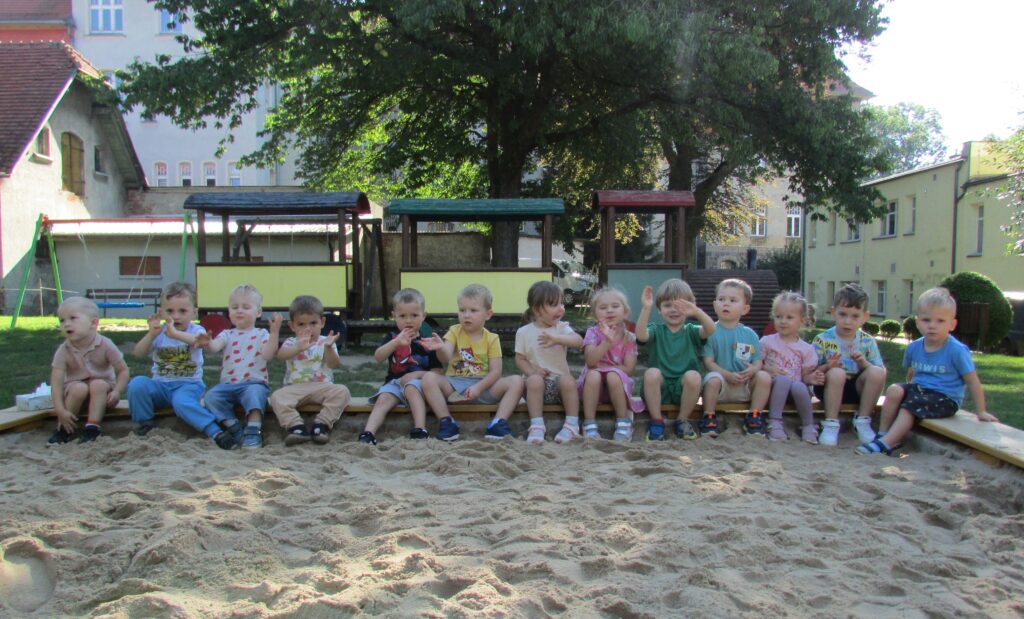 Dzieci siedzące w rzędzie na brzegu piaskownicy. 