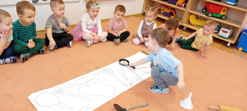 Dzieci podczas zajęć dywanowych- dopasowują przedmioty kuchenne do narysowanego szablonu.