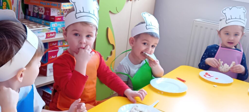 Dzieci przy stoliku podczas jedzenia własnoręcznie zrobionej kanapki z twarożkiem.