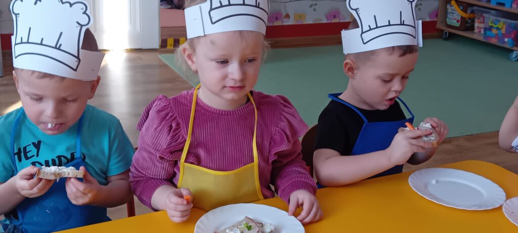 Dzieci przy stoliku podczas jedzenia pieczywa twarożkiem.