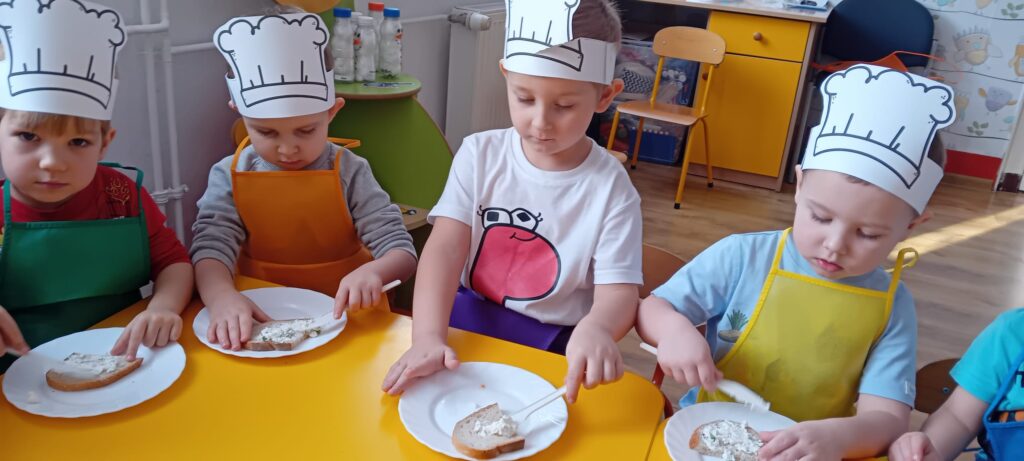 Dzieci przy stoliku podczas smarowania pieczywa twarożkiem.