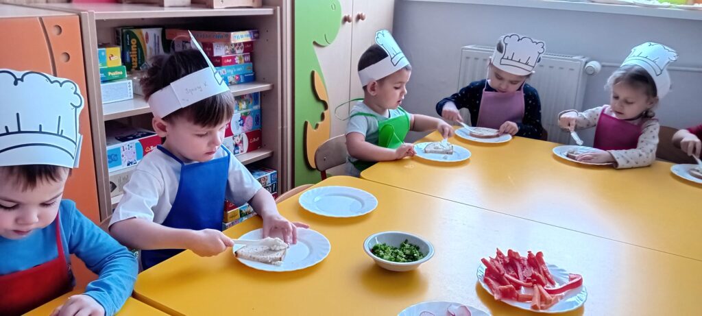 Dzieci przy stoliku podczas smarowania pieczywa twarożkiem.