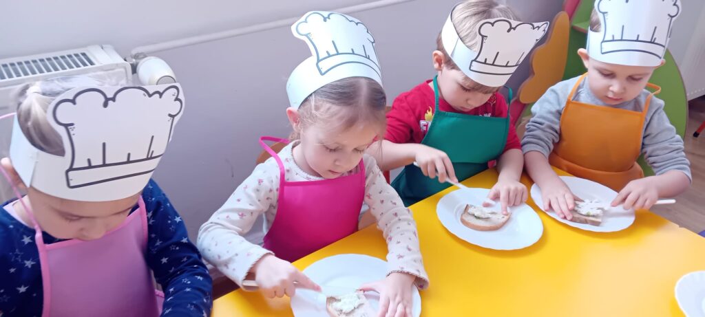 Dzieci przy stoliku podczas smarowania pieczywa twarożkiem.