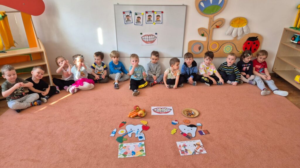 Dzieci siedzą na dywanie- dobierają zdrowe produkty do szablonu zęba.